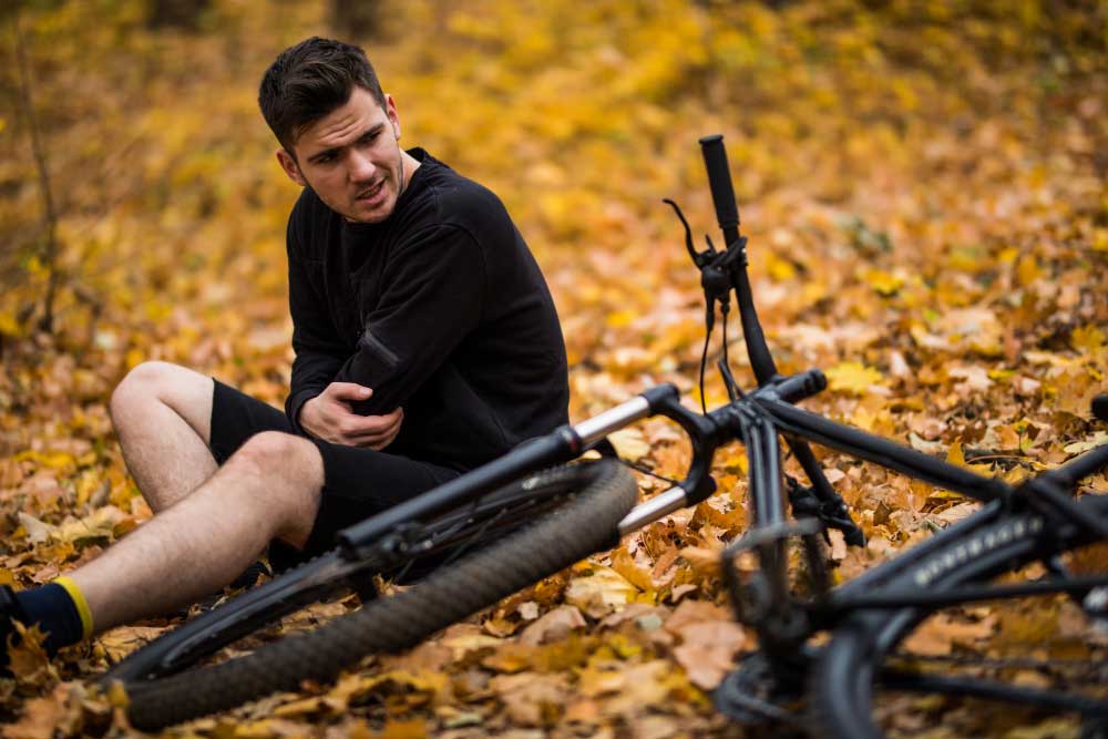 active young man holding by his hurt broken hands while lying autumn forest path by his bicycle Servicios Quiropracticos Servicios Quiropracticos Servicios Quiropracticos